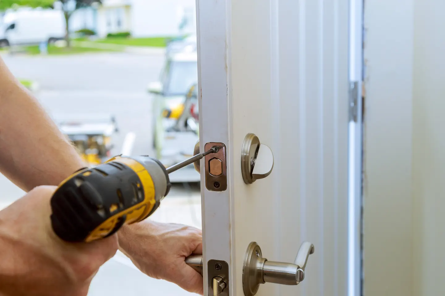 Locksmith fitting a new deadbolt and lever set on a white front door with a drill
